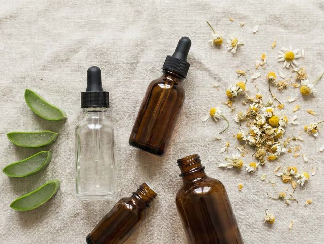A collection of natural skincare ingredients including aloe vera, chamomile, and botanical oils on a light pink linen surface.