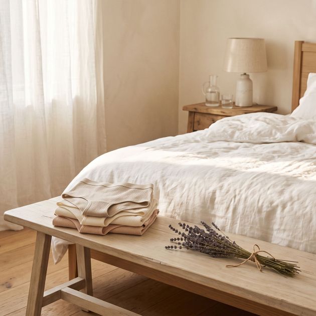 Soft white cotton bed linens in morning light with folded natural cotton underwear, representing breathable, underwear-free sleep for intimate skin
