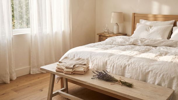 Soft white cotton bed linens in morning light with folded natural cotton underwear, representing breathable, underwear-free sleep for intimate skin