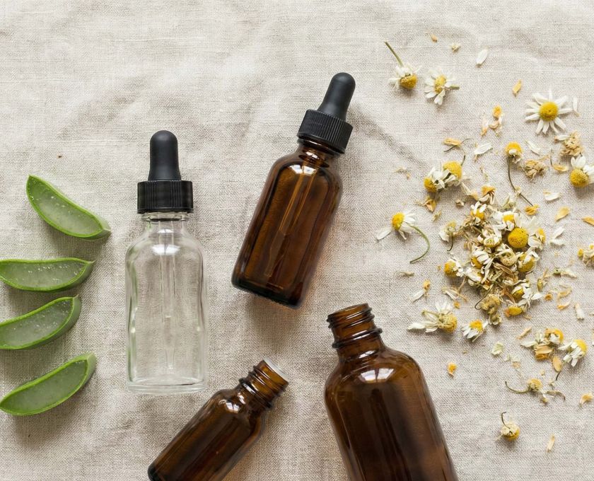 Une collection d'ingrédients de soin naturels comprenant de l'aloe vera, de la camomille et des huiles botaniques sur une surface en lin rose clair.