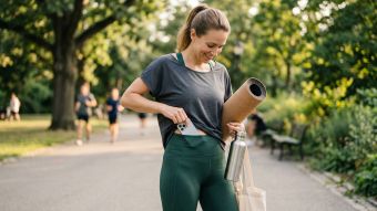 Eine Frau in salbeigrünen Leggings steckt ihr Smartphone beim Spaziergang in den Bund.