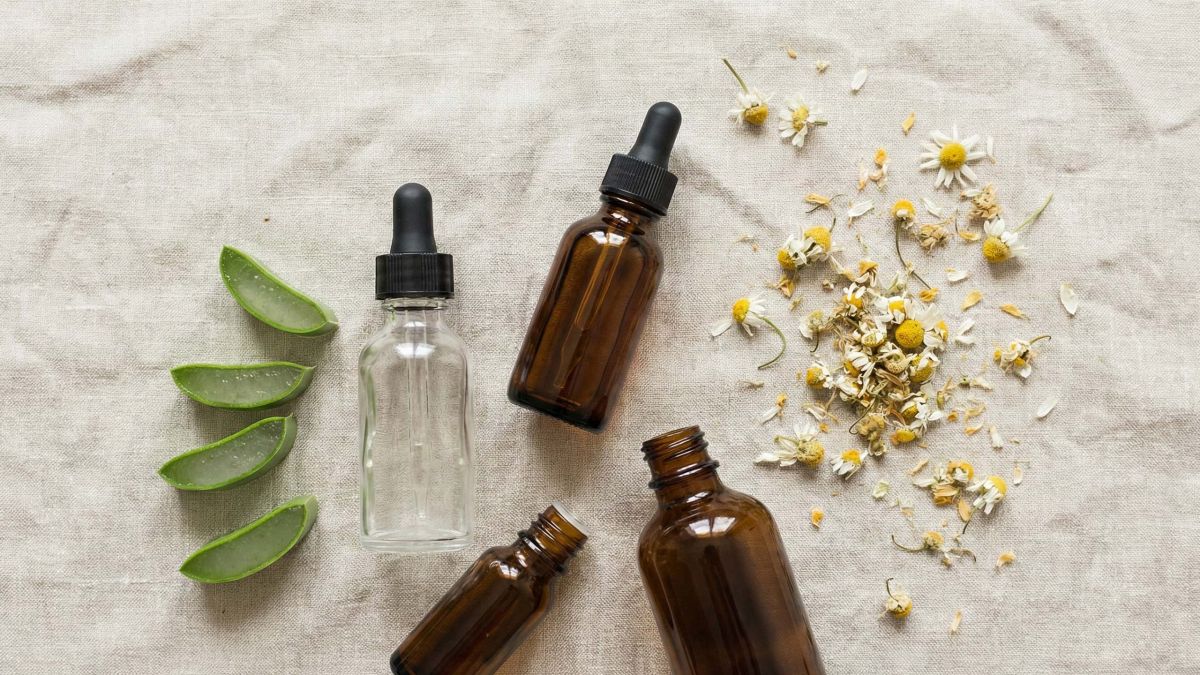 Uma coleção de ingredientes naturais para o cuidado da pele, incluindo aloe vera, camomila e óleos botânicos, sobre uma superfície de linho rosa claro.