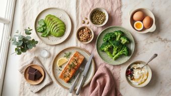 A flat-lay of foods that support hormonal balance including avocado, salmon, eggs, walnuts, and dark chocolate on a linen surface