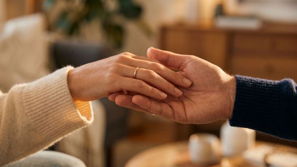 A woman's hand gently resting in a man's hand in soft warm light, expressing romantic love through touch