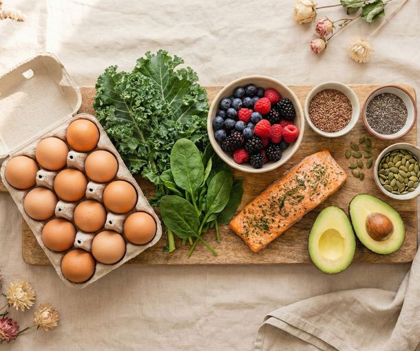 A selection of whole foods that support hormonal balance in women, including eggs, leafy greens, berries, fish, and seeds.