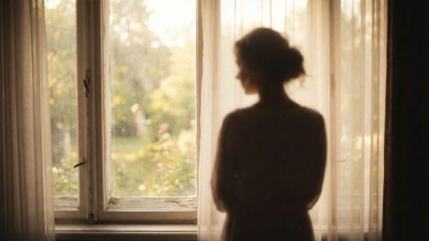 Una mujer mirando pensativa por una ventana, símbolo de reflexión personal y sanación emocional.