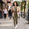 A stylish woman walking down a city sidewalk wearing olive green activewear and a beige jacket.