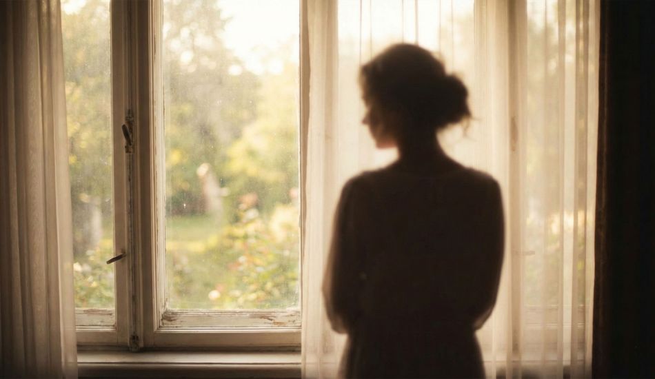 Una mujer mirando pensativa por una ventana, símbolo de reflexión personal y sanación emocional.