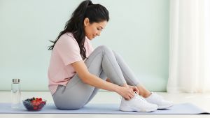 Mujer ata sus zapatillas junto a frutos rojos y agua—hábitos equilibrados y sostenibles