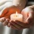 Hands holding a small lit candle beside a cozy blanket on a table